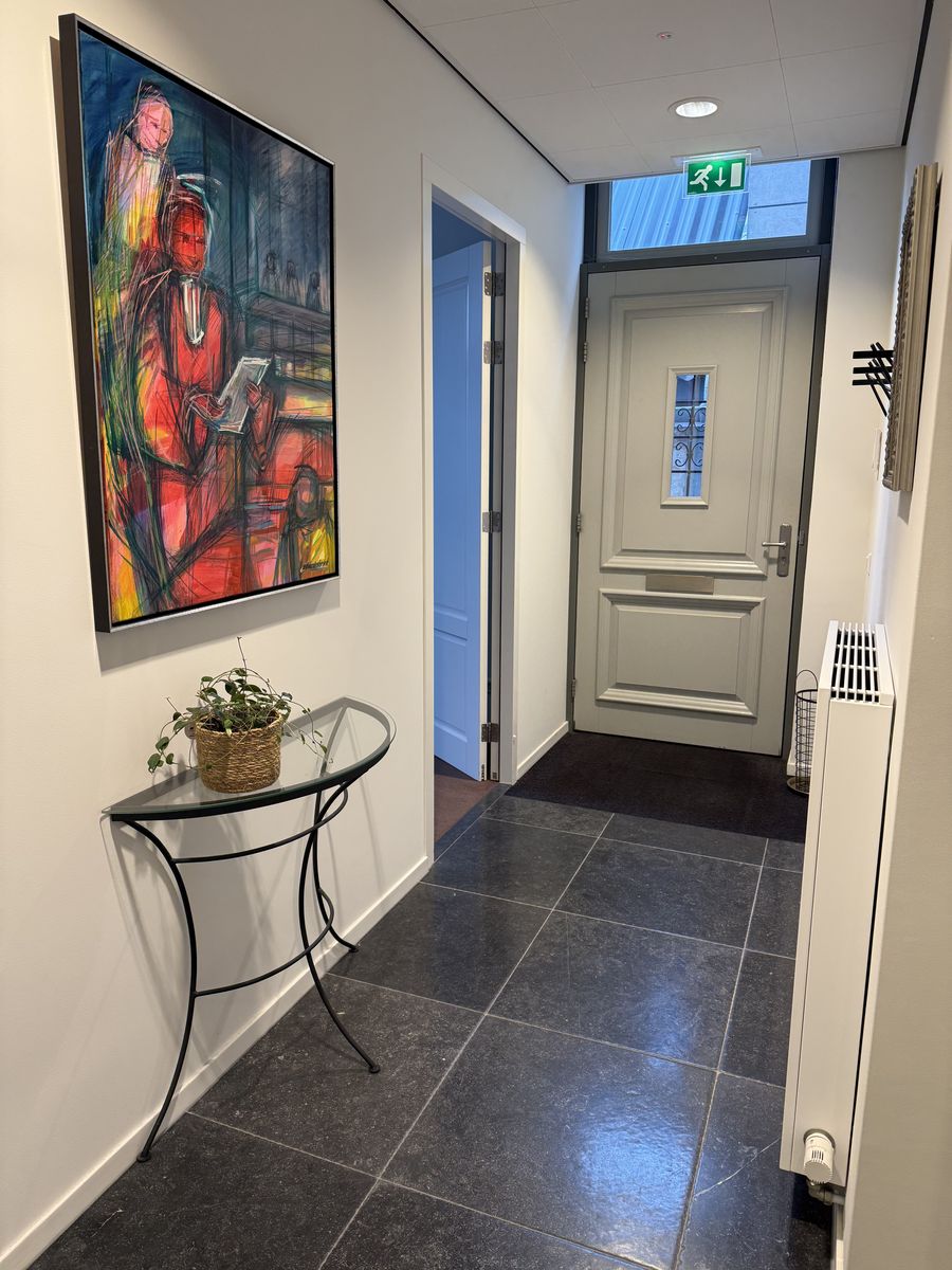De gang van het kantoor, met een schilderij aan de wand en de voordeur achterin